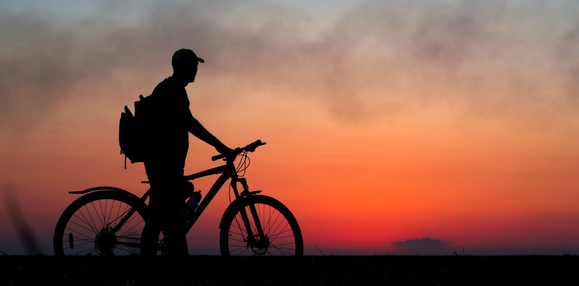 Silhouette of cyclist on the background of red sunset. Biker with bicycle on the field during sunrise